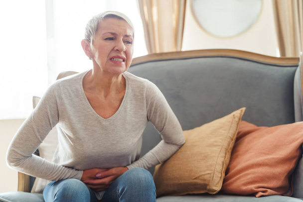 Modern senior woman experiencing severe stomach spasms - 写真・画像