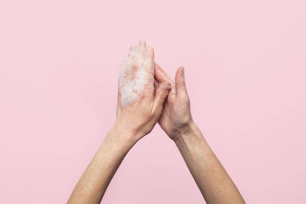 Hand washing. Soapy female hands on a pink background. Concept of the rules of washing and handling hands. Top view, flat lay. - Photo, image