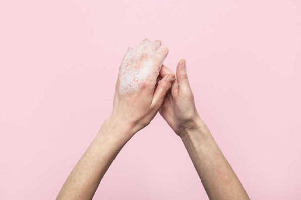 Hand washing. Soapy female hands on a pink background. Concept of the rules of washing and handling hands. Top view, flat lay. - 写真・画像