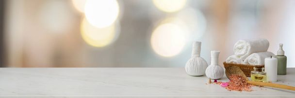 Oříznutý záběr lázeňského příslušenství s bílým ručníkem, lázeňskou solí, aromatickým olejem, bylinnými kompresními koulemi a kopírovacím prostorem na mramorovém stole - Fotografie, Obrázek