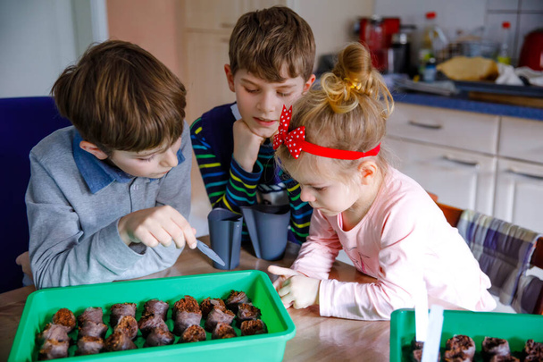 Two kid boys and little toddler girl planting vegetable seeds at home. Three siblings watering together ground in boxes and seeding tomatoes in organic greenhouse. Family agrdening and farming - Фото, зображення
