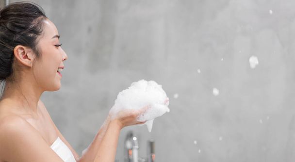Портрет усміхненої щасливої красивої красивої азіатки чиста свіжа здорова біла шкіра насолоджується розслаблюючим прийомом душу та ванни з мильною піною у ванній кімнаті
 - Фото, зображення