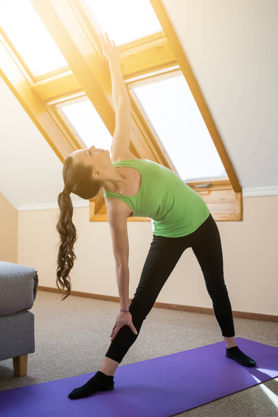 Mladá žena doma cvičí jógu. Trikonasana / bikram trojúhelník vpravo - Fotografie, Obrázek