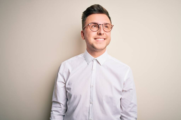 Young handsome business mas wearing glasses and elegant shirt over isolated background looking away to side with smile on face, natural expression. Laughing confident. - Photo, Image