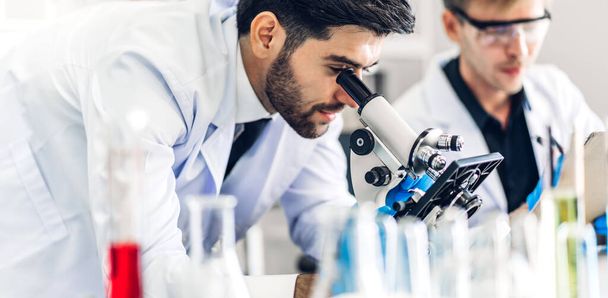 Professional scientist man research and working with microscope.Young science man doing a chemical experiment while making analyzing and mixing chemicals liquid in glassware at biomedical laboratory - Foto, immagini