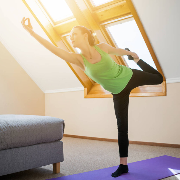Young woman is practicing yoga at home. Natarajasana / Shiva posture pose - Photo, Image