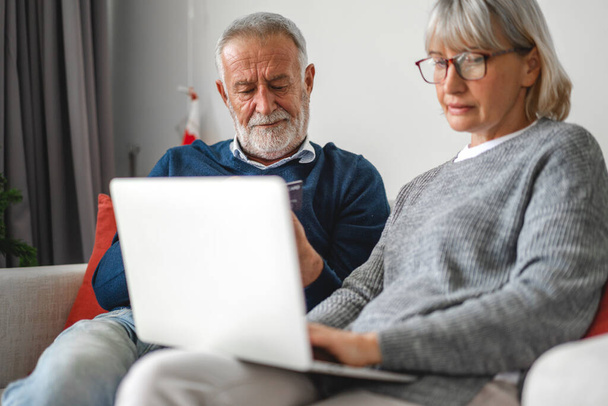 Счастливые пожилые муж и жена, проверяя социальные сети и читая новости или покупки в Интернете, сидя на диване в home.Retirement концепции - Фото, изображение