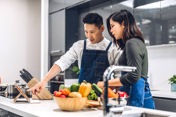 Young asian family couple having fun cooking together with fresh vegetable salad on table.Happy couple looking for recipe on Internet with tablet computer to prepare the yummy eating lunch in kitchen - Фото, зображення
