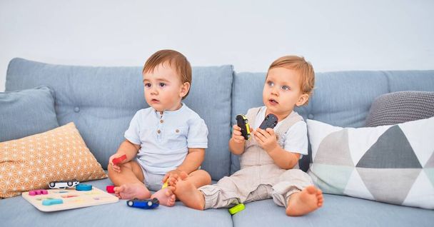 Beautiful toddlers sitting on the sofa playing with toys at home - Photo, Image