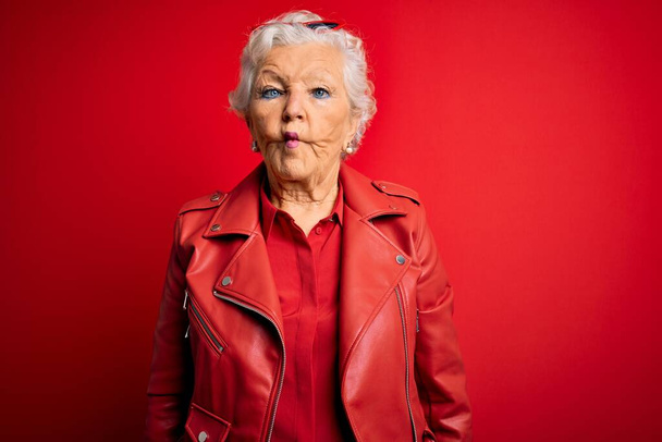 Senioren mooie grijsharige vrouw met casual rode jas en zonnebril vissengezicht met lippen, gek en komisch gebaar. Grappige uitdrukking.. - Foto, afbeelding