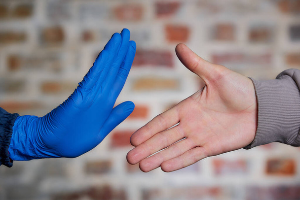 Egy férfi meztelen kézzel felajánlja, hogy kezet fog egy nővel. Egy nő kezével eldobható orvosi kesztyűben megállítja, hogy elkerülje a koronavírus terjedését (COVID-19). Nem akar kezet fogni..  - Fotó, kép