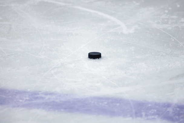 Un vecchio disco da hockey su ghiaccio nero sul ghiaccio vicino alla linea blu. Foto scattata in Lettonia
. - Foto, immagini