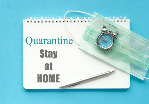 Coronavirus Covid -19 quarantine concept. Stay at home, work at home. Notebook, medical mask, clock on blue background. top view. Copy space - Zdjęcie, obraz