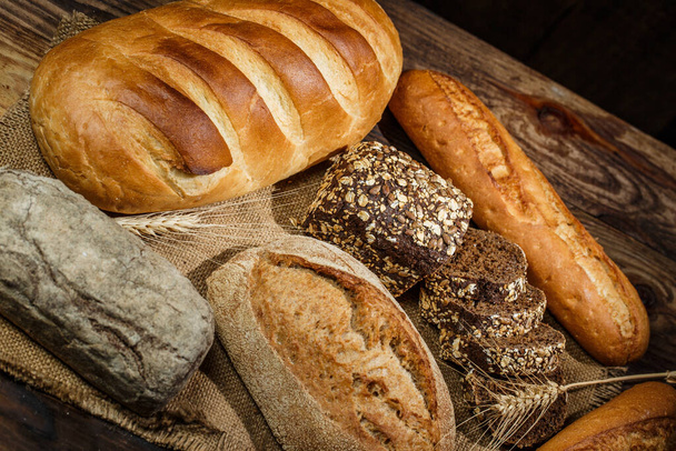 Čerstvé bochníky chleba s pšenicí a lepkem na dřevěném stole - Fotografie, Obrázek