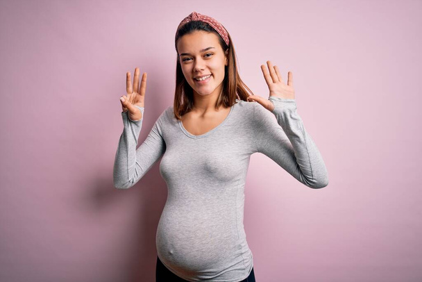 Young beautiful teenager girl pregnant expecting baby over isolated pink background showing and pointing up with fingers number eight while smiling confident and happy. - Photo, Image