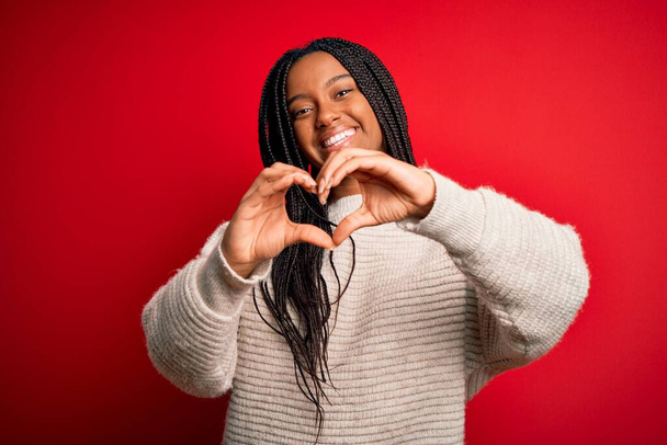 Jonge Afro-Amerikaanse vrouw draagt casual winter trui over rood geïsoleerde achtergrond glimlachend in liefde doen hart symbool vorm met handen. Romantisch concept. - Foto, afbeelding