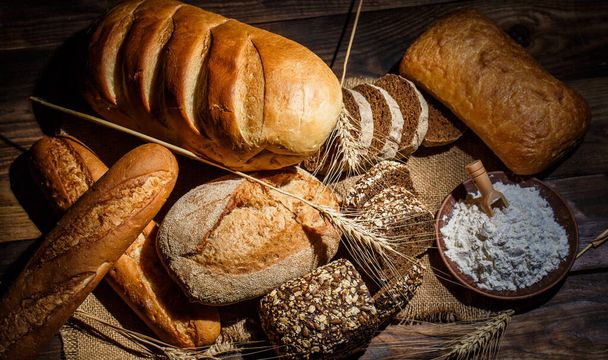 Fresh loaves of bread with wheat and gluten on a wooden table - Foto, imagen