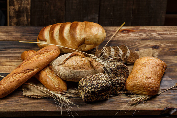 Fresh loaves of bread with wheat and gluten on a wooden table - Foto, Imagem
