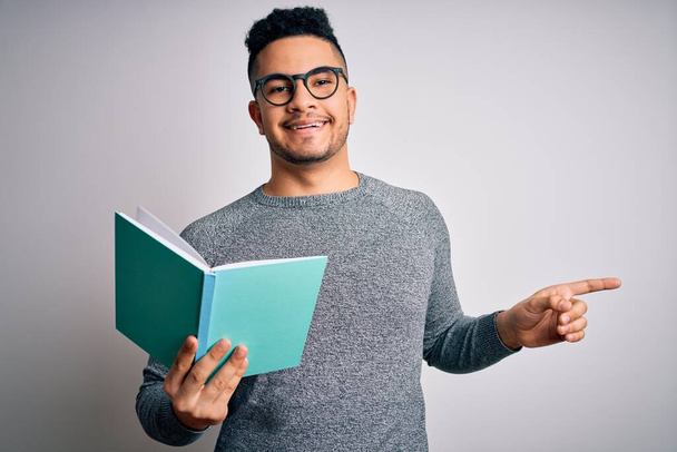 Nuori komea fiksu opiskelija mies lukee kirjaa yli eristetty valkoinen tausta erittäin onnellinen osoittaa käsin ja sormella sivulle
 - Valokuva, kuva