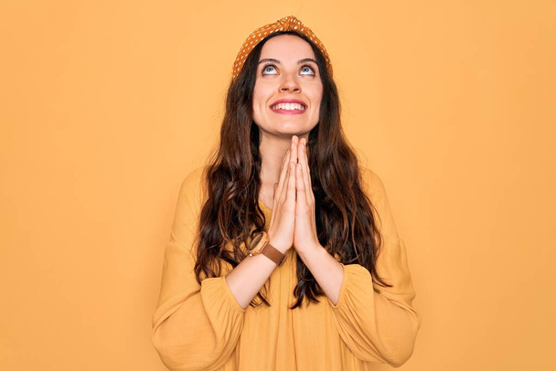 Young beautiful woman wearing casual t-shirt and diadem standing over yellow background begging and praying with hands together with hope expression on face very emotional and worried. Begging. - Photo, Image