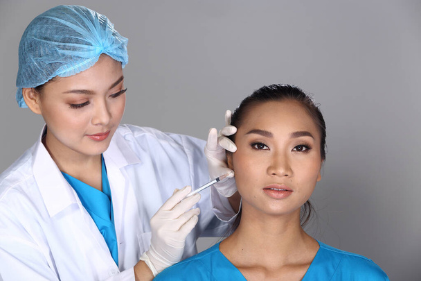 Médico asiático Enfermera comprobar la estructura del hueso de la mejilla de la cara antes de la cirugía plástica e inyectar jeringa química de belleza para el paciente con acné, verruga, Studio iluminación fondo gris
 - Foto, imagen