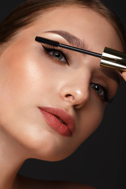 Beautiful girl with sexy lips and classic makeup with cosmetic mascara brush in hand. Beauty face. - Photo, image