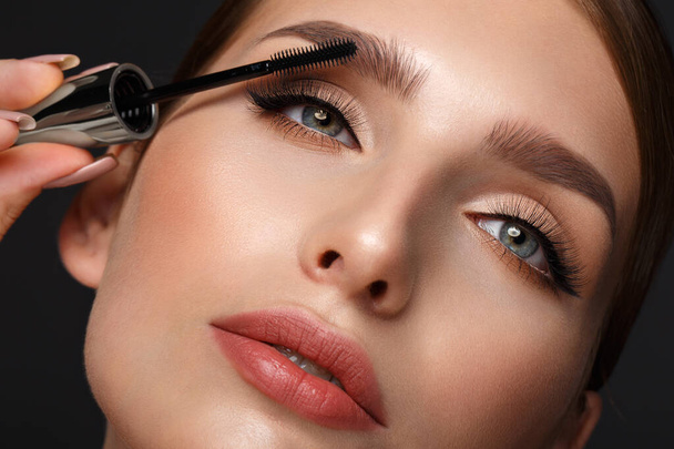 Beautiful girl with sexy lips and classic makeup with cosmetic mascara brush in hand. Beauty face. - Zdjęcie, obraz