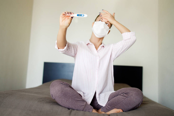 Sick girl in medical mask with thermometer in hand . Coronavirus epidemic - Фото, зображення