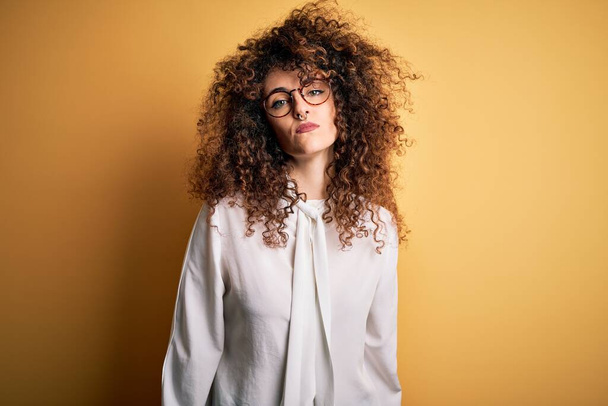 Young beautiful brunette woman with curly hair and piercing wearing shirt and glasses Relaxed with serious expression on face. Simple and natural looking at the camera. - Photo, Image