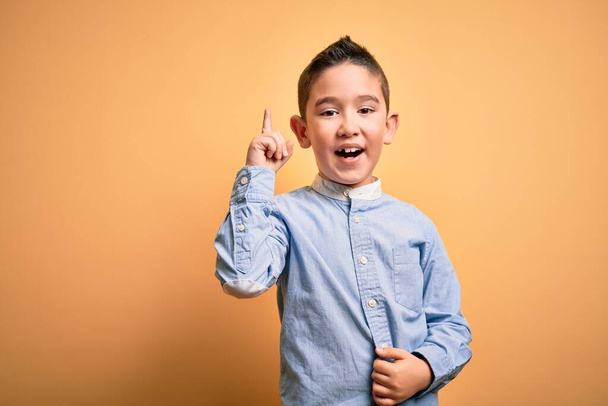 Маленький мальчик в элегантной рубашке, стоящей на желтом изолированном фоне, указывая пальцем на успешную идею. Взволнован и счастлив. Номер один
. - Фото, изображение
