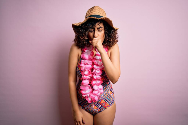 Jeune belle femme arabe en vacances portant un maillot de bain et des fleurs de lei hawaïen se sentant mal et toussant comme symptôme de rhume ou de bronchite. Concept de soins de santé
. - Photo, image