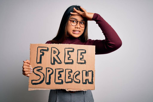 Asian girl asking for rights holding banner with free speech message over white background stressed with hand on head, shocked with shame and surprise face, angry and frustrated. Fear and upset for mistake. - Foto, imagen