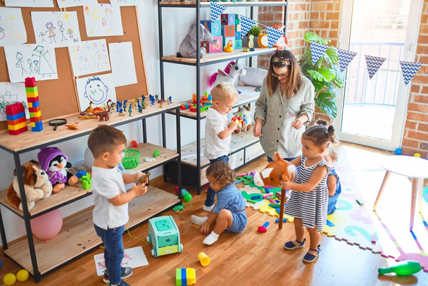 Piękny nauczyciel i grupa maluchów bawiących się wokół mnóstwo zabawek w przedszkolu - Zdjęcie, obraz