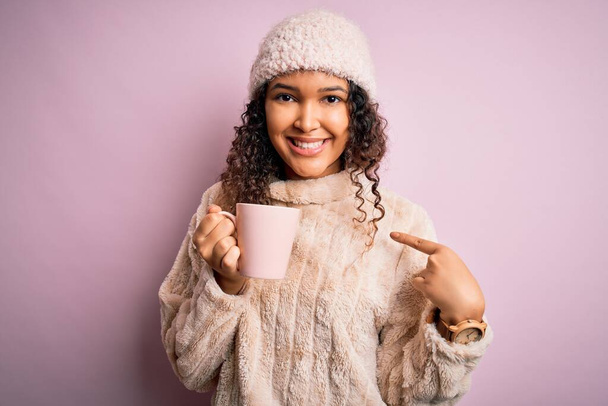 Joven hermosa mujer con pelo rizado beber taza de café sobre fondo rosa aislado con la cara sorpresa señalando dedo a sí mismo
 - Foto, imagen