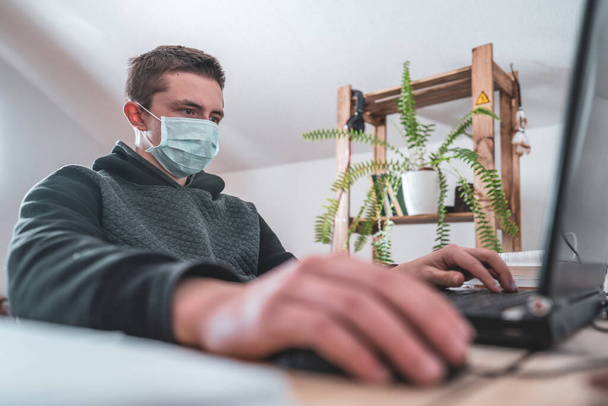Active teen Boy in face mask with laptop homework during a coronavirus quarantine. concept of online education. Social distance, self- isolation. Distance learning due to virus, flu, epidemic COVID-19 - Photo, Image
