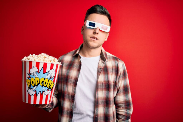 Young handsome caucasian man wearing 3d movie glasses and eating popcorn looking sleepy and tired, exhausted for fatigue and hangover, lazy eyes in the morning. - Foto, Imagen