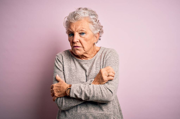 Senior mooie vrouw dragen casual t-shirt staan over geïsoleerde roze achtergrond schudden en bevriezen voor de winter koud met droevige en schok uitdrukking op gezicht - Foto, afbeelding