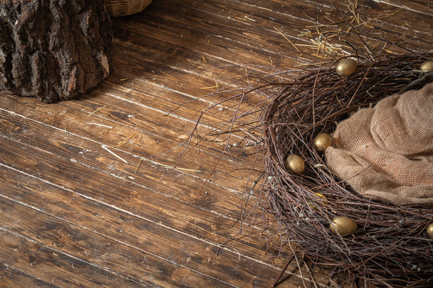 Happy Easter! Easter decoration. A nest of willow branches with Golden eggs on the brown wooden floor. The view from the top. Sacking is laid in the nest . Copy spase for text. - Photo, Image