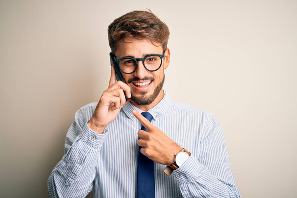 白い背景の上でスマートフォンで会話をしている若いビジネスマンは手と指で非常に幸せなポインティング - 写真・画像