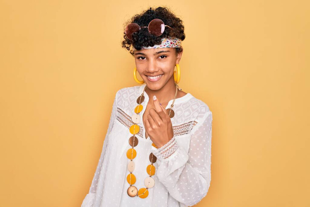 Jeune belle afro afro américaine hippie femme portant des lunettes de soleil et accessoires Beckoning venir ici geste avec la main invitant accueillant heureux et souriant
 - Photo, image