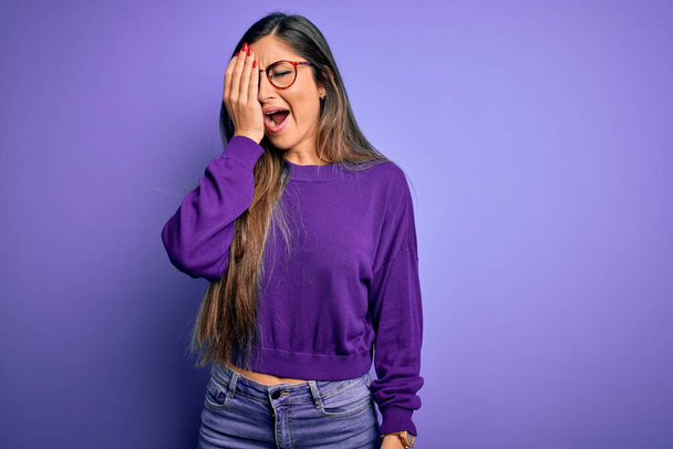 Young beautiful smart woman wearing glasses over purple isolated background Yawning tired covering half face, eye and mouth with hand. Face hurts in pain. - Photo, Image