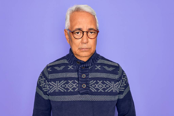 Középkorú, ősz hajú férfi szemüvegben és téli pulóverben a lila háttér szkeptikus és ideges, rosszalló feldúlt a probléma miatt. Negatív személy. - Fotó, kép