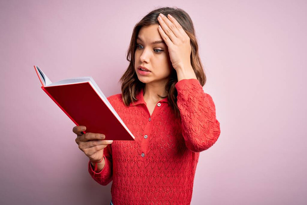 Young blonde student girl reading a book over pink  isolated background stressed with hand on head, shocked with shame and surprise face, angry and frustrated. Fear and upset for mistake. - Foto, Bild