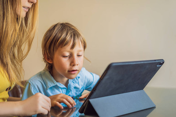 Un chico que estudia en línea en casa usando una tableta. Mamá le ayuda a aprender. Estudiar durante la cuarentena. Virus covidémico pandémico global19
 - Foto, Imagen