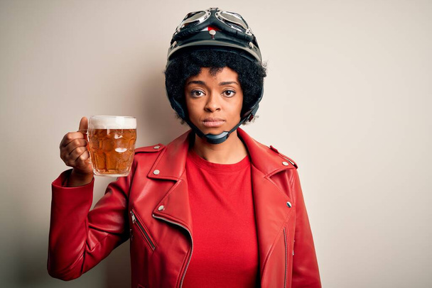 Young African American afro motorcyclist woman with curly hair drinking jar of beer with a confident expression on smart face thinking serious - Photo, Image
