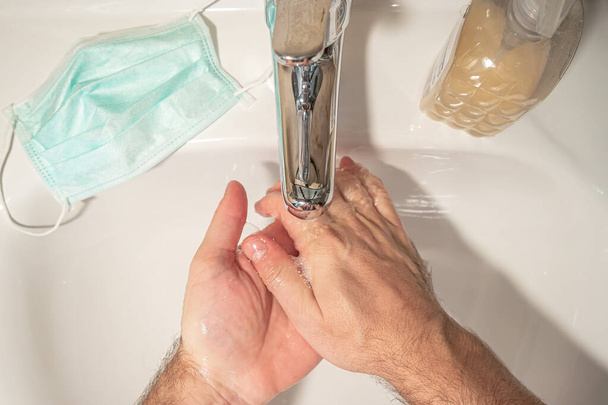 Yukarıdan bakıldığında, tuvalette sıvı sabunla yıkanan eller, dünya çapında koronavirüs salgınını ve tıbbi maskeyi önlemek için alınan önlemler. - Fotoğraf, Görsel
