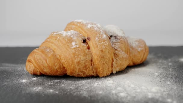 Frisches Croissant mit Schokolade und Zuckerpulver rotiert auf einer schwarzen Tafel auf einem weißen Tisch. Konzept, zu Hause zu bleiben und sich gesund zu ernähren Leckeres Frühstück. Ansicht von oben. 4K - Filmmaterial, Video