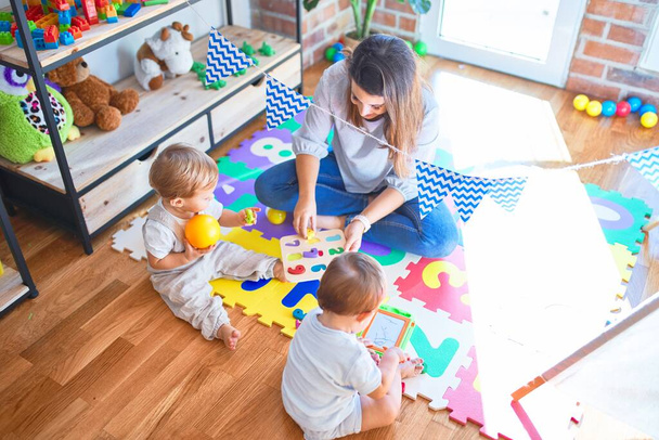 Красивий вчитель і малюки грають навколо багато іграшок в дитячому саду
 - Фото, зображення