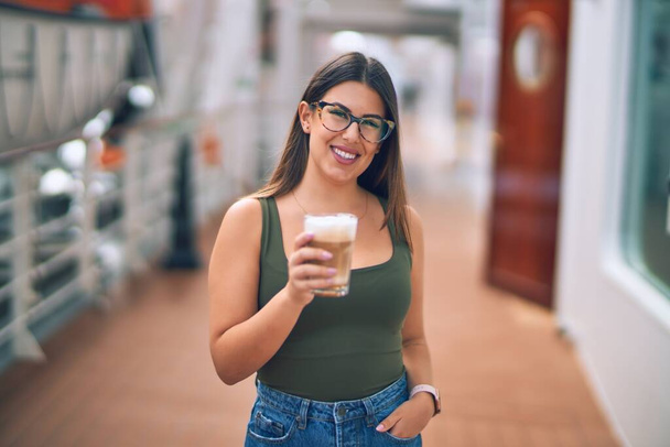 休暇中の若い美しい女性が幸せと自信を笑顔。コーヒーを飲みながら笑顔で船のデッキに立ちクルーズをする - 写真・画像