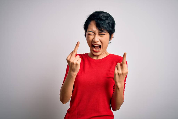 Молода красива азіатська дівчина в повсякденній червоній футболці, що стоїть над ізольованим білим тлом, показує середній палець робить вам погане вираження, провокації та грубе ставлення. Крик збуджений
 - Фото, зображення